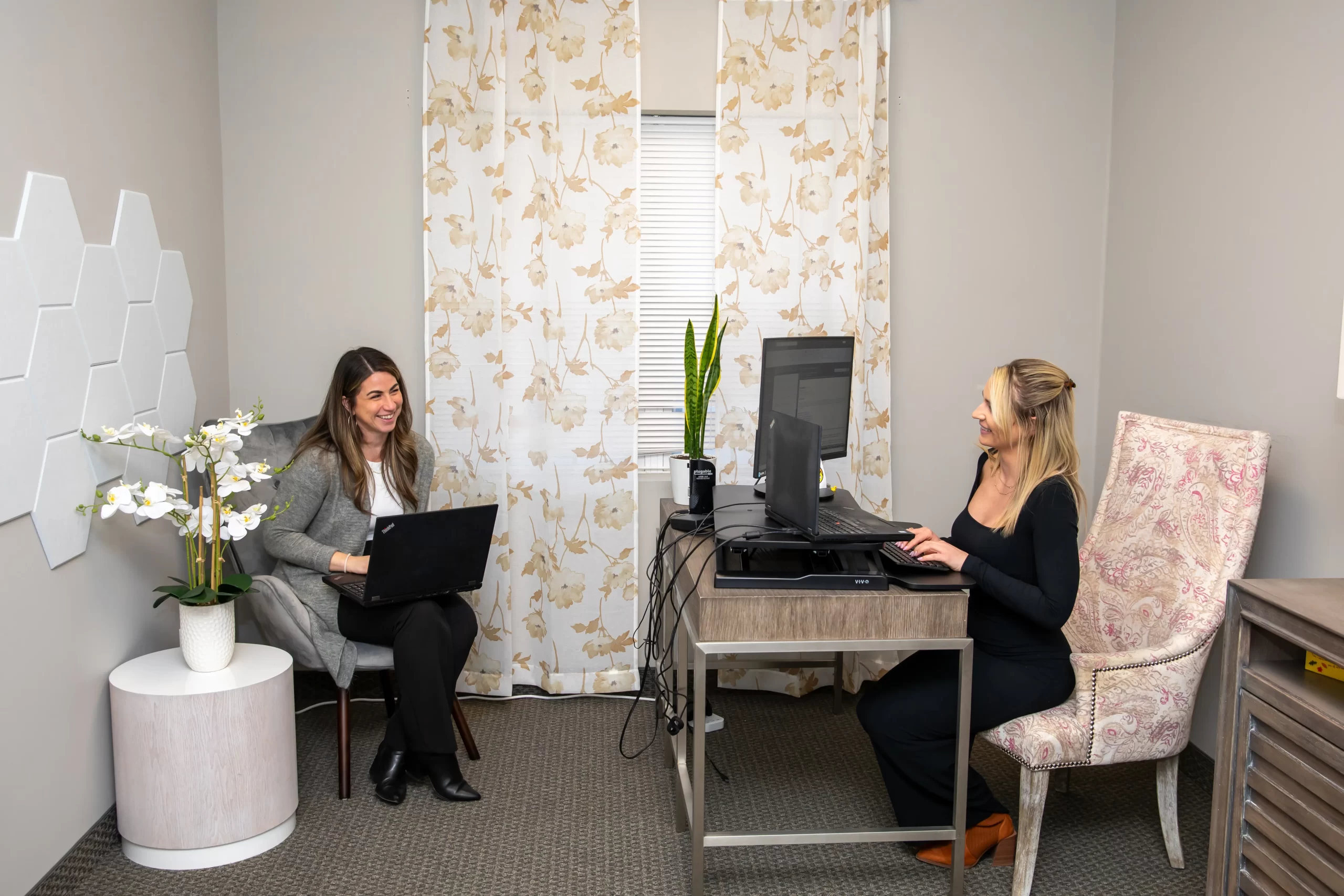Two business professionals working on laptops in private office workspace